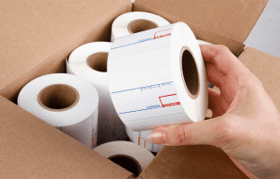 An open box containing 6 rolls of preprinted UPC scale labels and a hand picking up one of the rolls