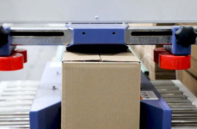 A box being sealed and then rolling down a conveyor before being picked up by a person